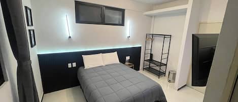 Un dormitorio moderno con una cama, un televisor montado en la pared, un estante colgante y un cesto de basura.