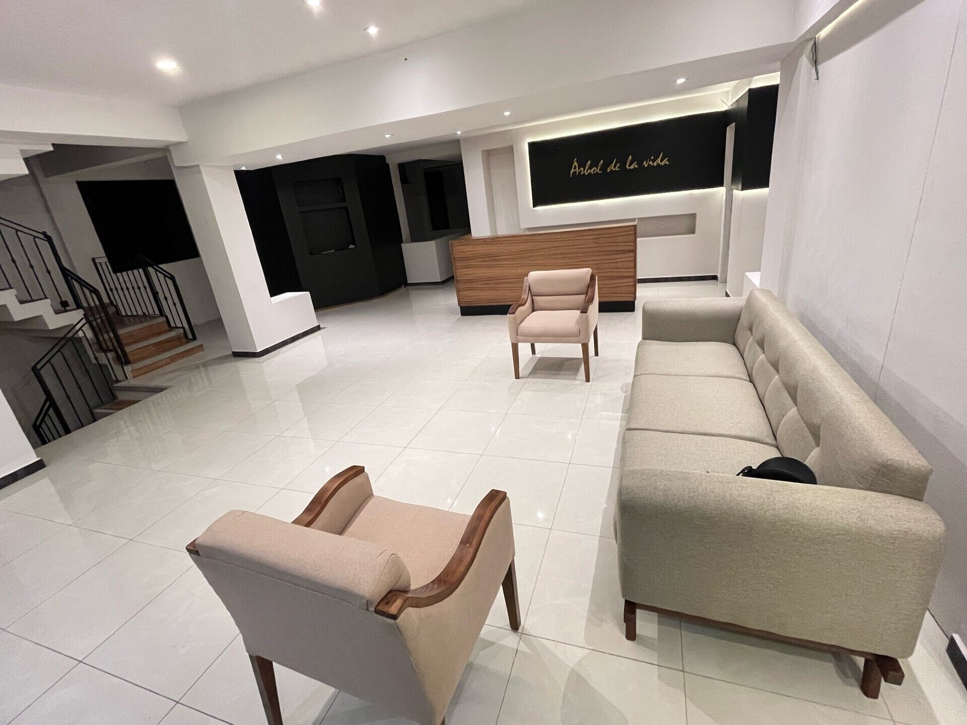 Un interior moderno con un sofá, dos sillones, un mostrador de recepción de madera y una escalera.