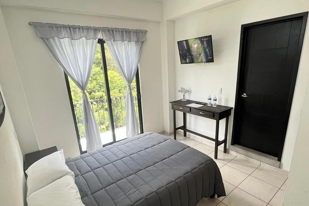 A bedroom with a bed, a desk, a TV, and a door.