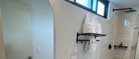 A modern bathroom with a large oval mirror, a wooden vanity, a white sink, a toilet, and a glass shower enclosure.