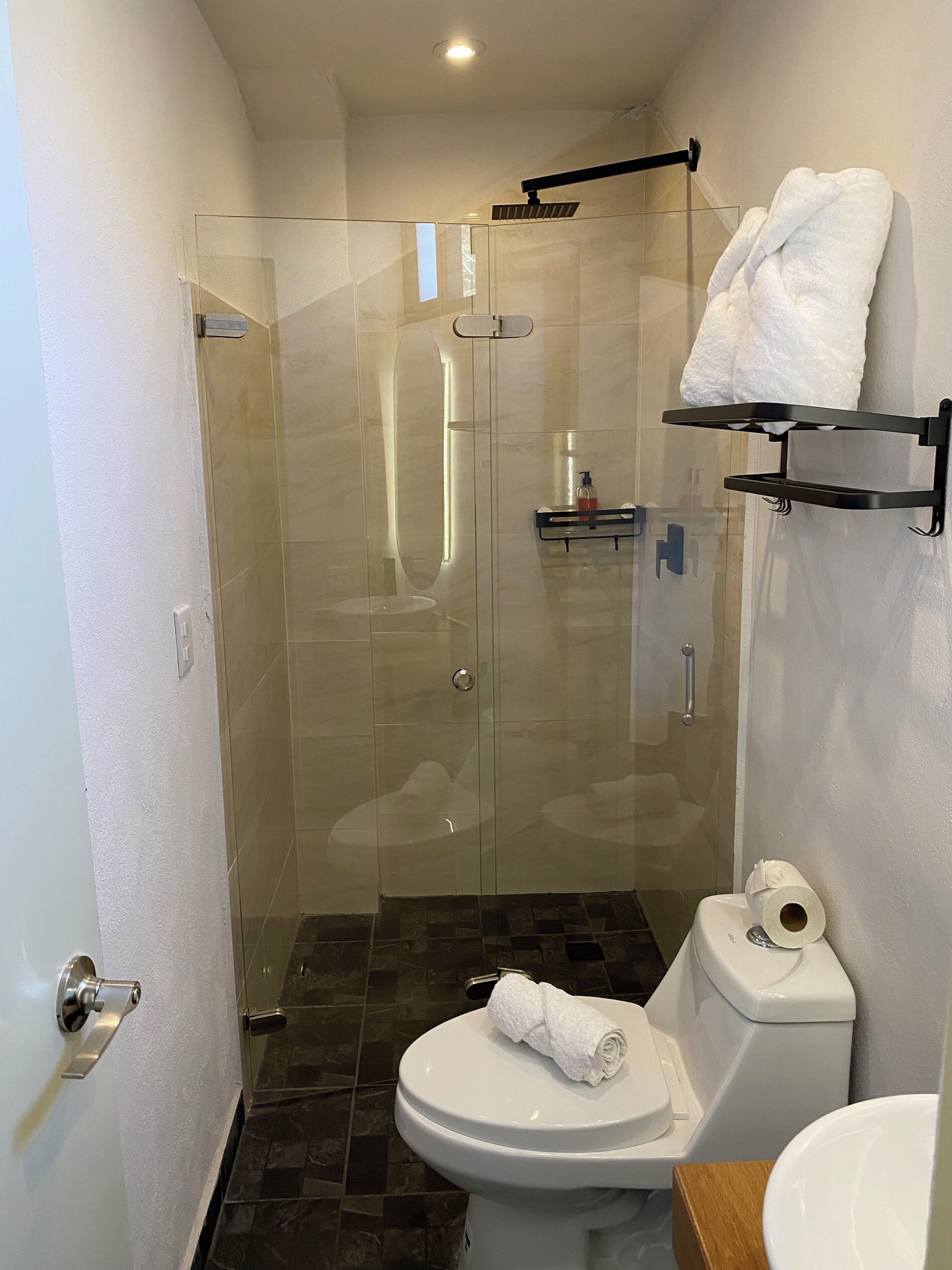 Een moderne badkamer met een douchecabine van glas, een toilet met een handdoek erop en een plank met toiletartikelen.
