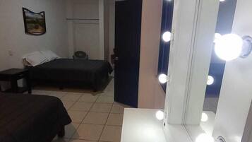 A hotel room with a bed, a bedside table, a mirror with lights, and a door.