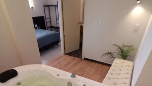A bathroom with a bathtub, a sink, and a mirror. There is a door leading to another room with a bed and a nightstand. - HOTEL BOUTIQUE ARBOL DE LA VIDA (Taxco)