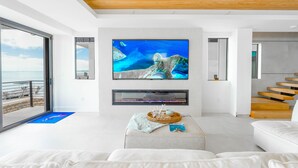 A modern living room with a large flat-screen TV mounted on a white wall, a wooden staircase, and a view of the ocean through large sliding doors. - 5 bed/4 bath Ocean side, right outside of Tavernier Creek Mile Marker 91 (Tavernier)