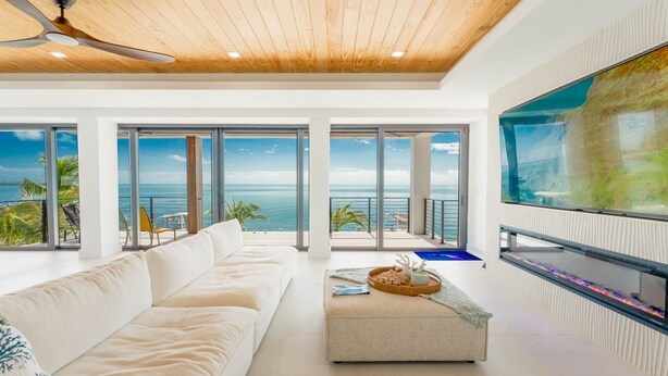 A modern living room with a large flat-screen TV, a white sofa, and a ceiling fan. - 5 bed/4 bath Ocean side, right outside of Tavernier Creek Mile Marker 91 (Tavernier)