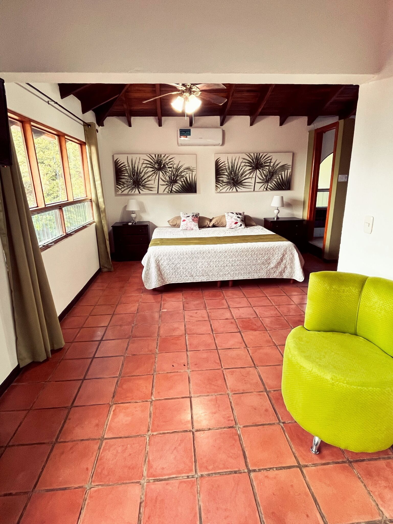 A bedroom with a bed, a bright green chair, a ceiling fan, and a window with curtains.