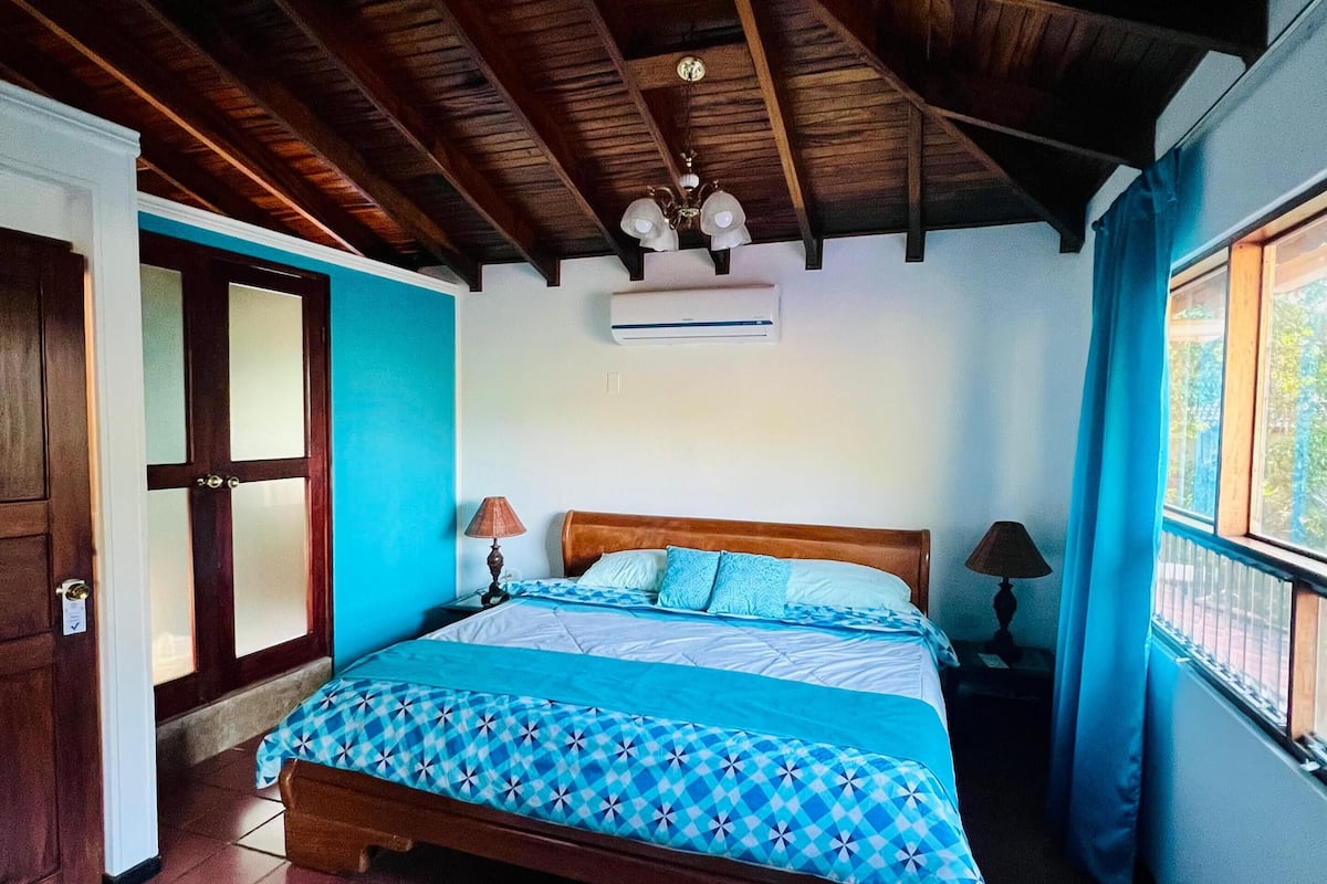 A bedroom with a wooden ceiling, a bed with a patterned bedspread, and a window with curtains.
