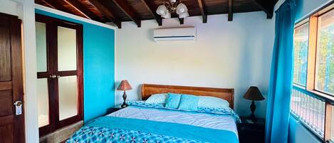 Un dormitorio con techo de madera, cama con colcha estampada y ventana con cortinas.