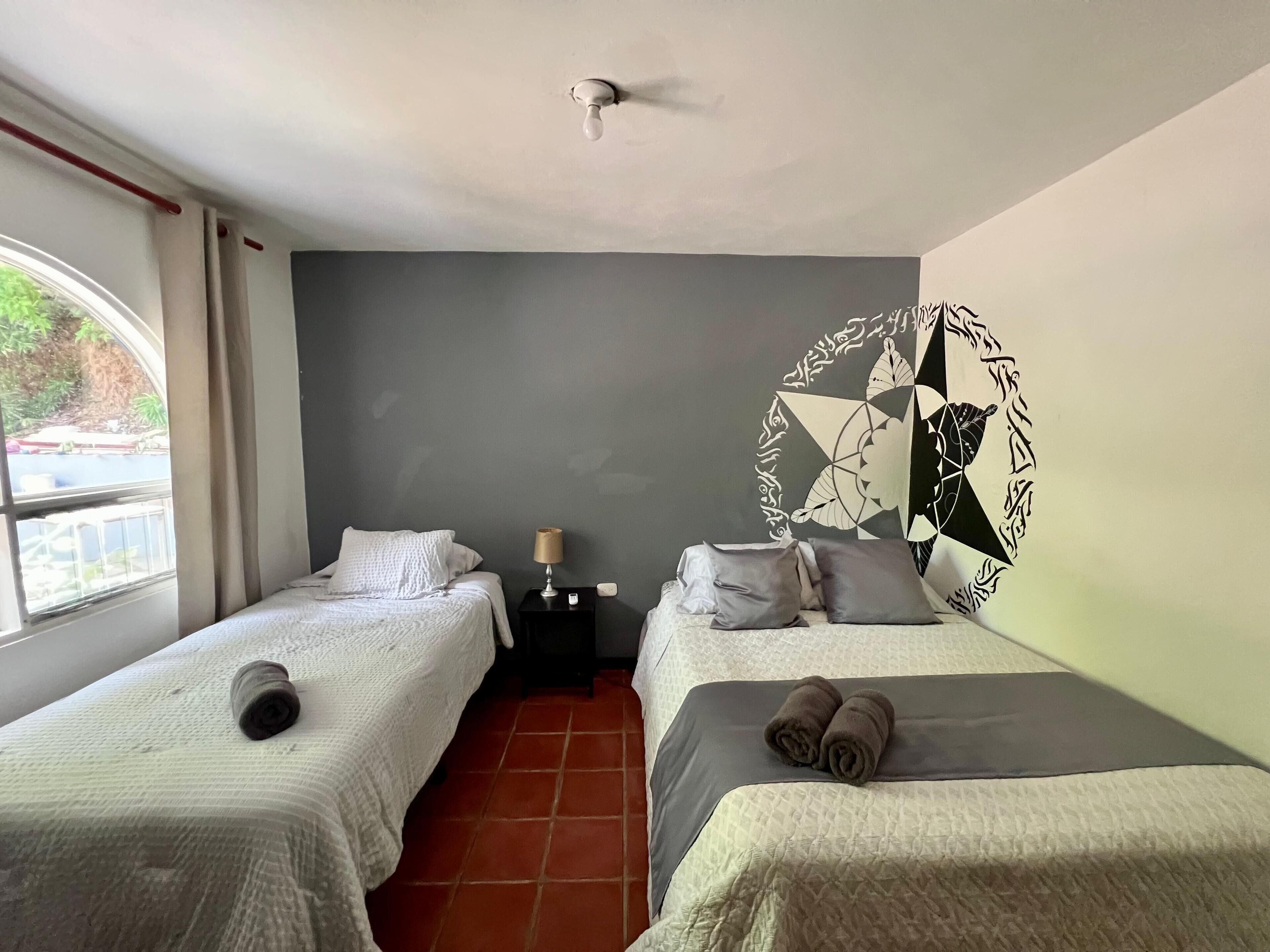 Habitación de hotel con dos camas, una mesita de noche, una lámpara y un adorno en la pared.