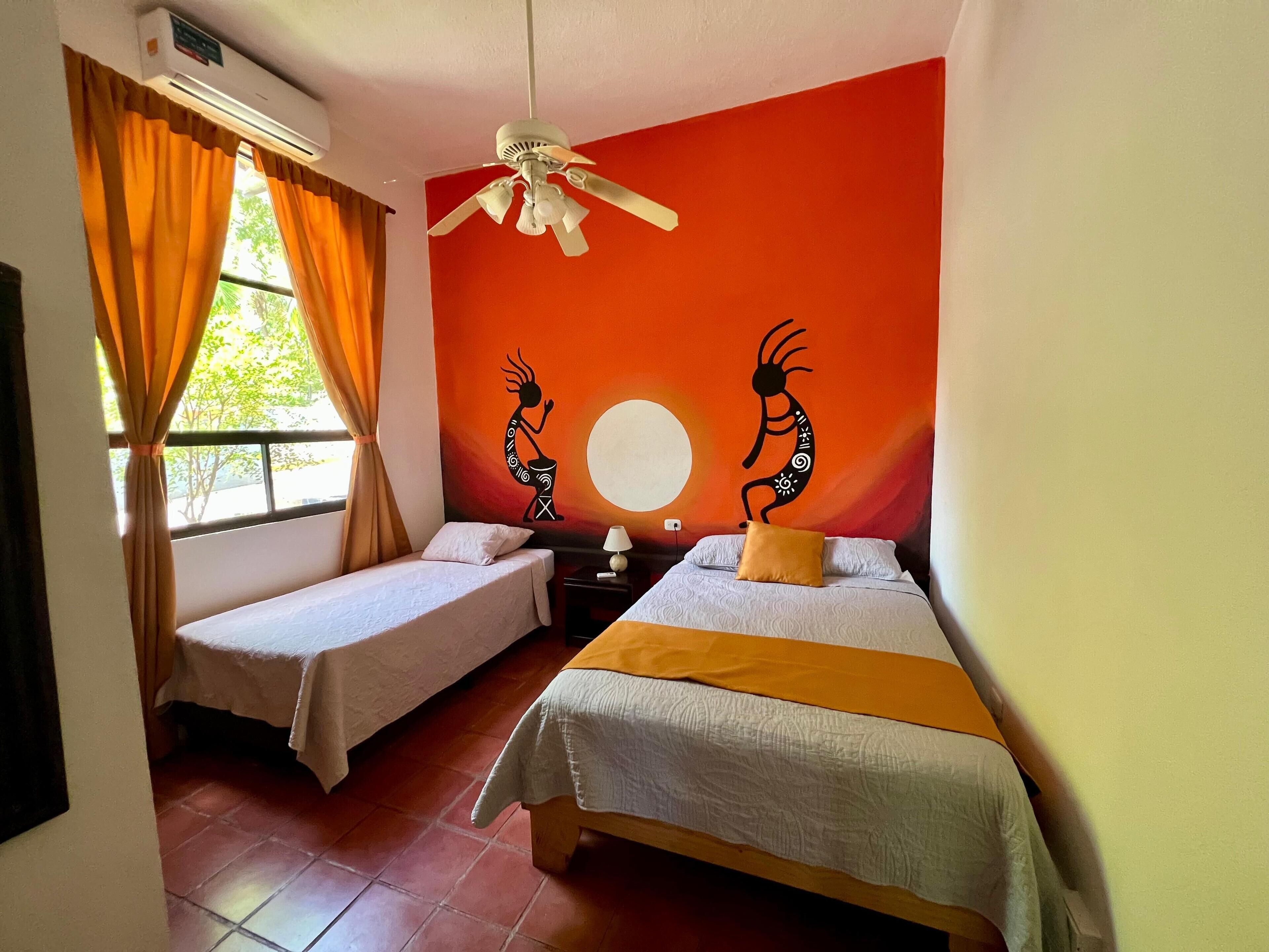 A room with two beds, a ceiling fan, and a wall mural.
