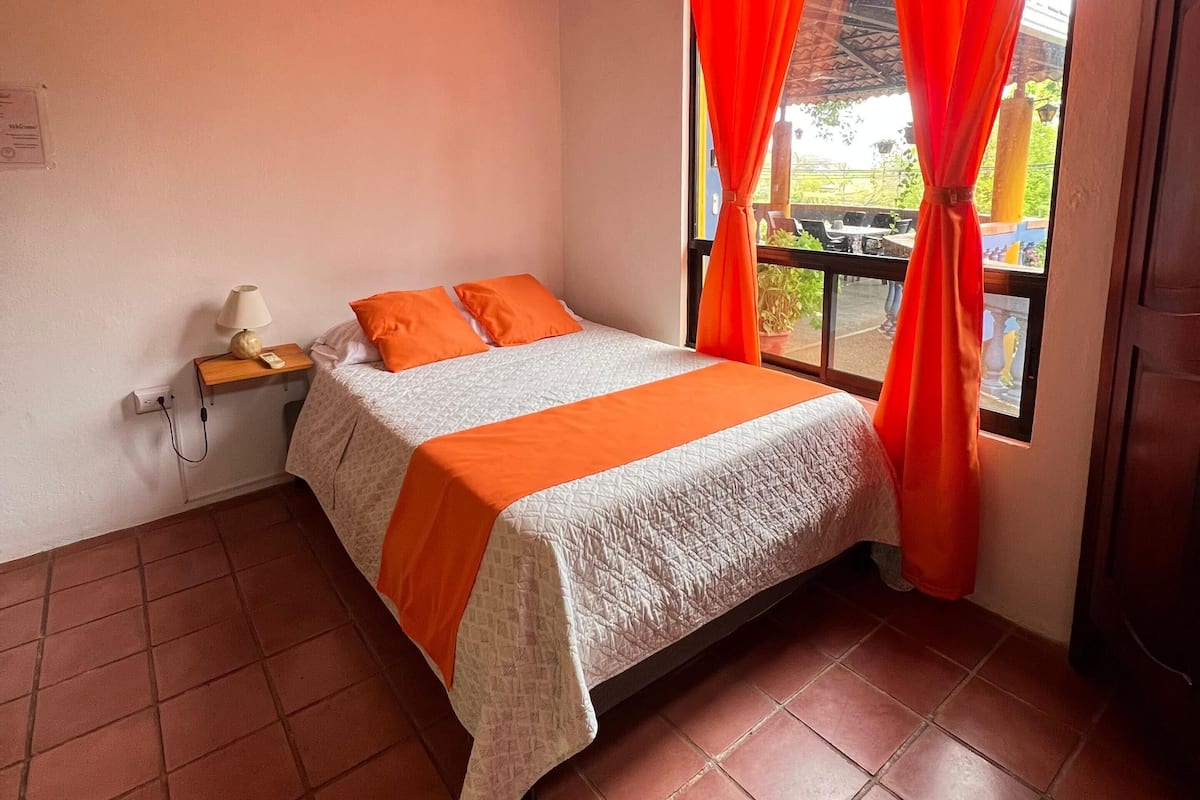 A bedroom with a bed, a nightstand, a ceiling fan, and a window with curtains.