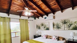 Ein Schlafzimmer mit Holzboden, einem Bett mit grüner Decke, einem Nachttisch mit Lampe und einem Fenster mit Vorhängen.