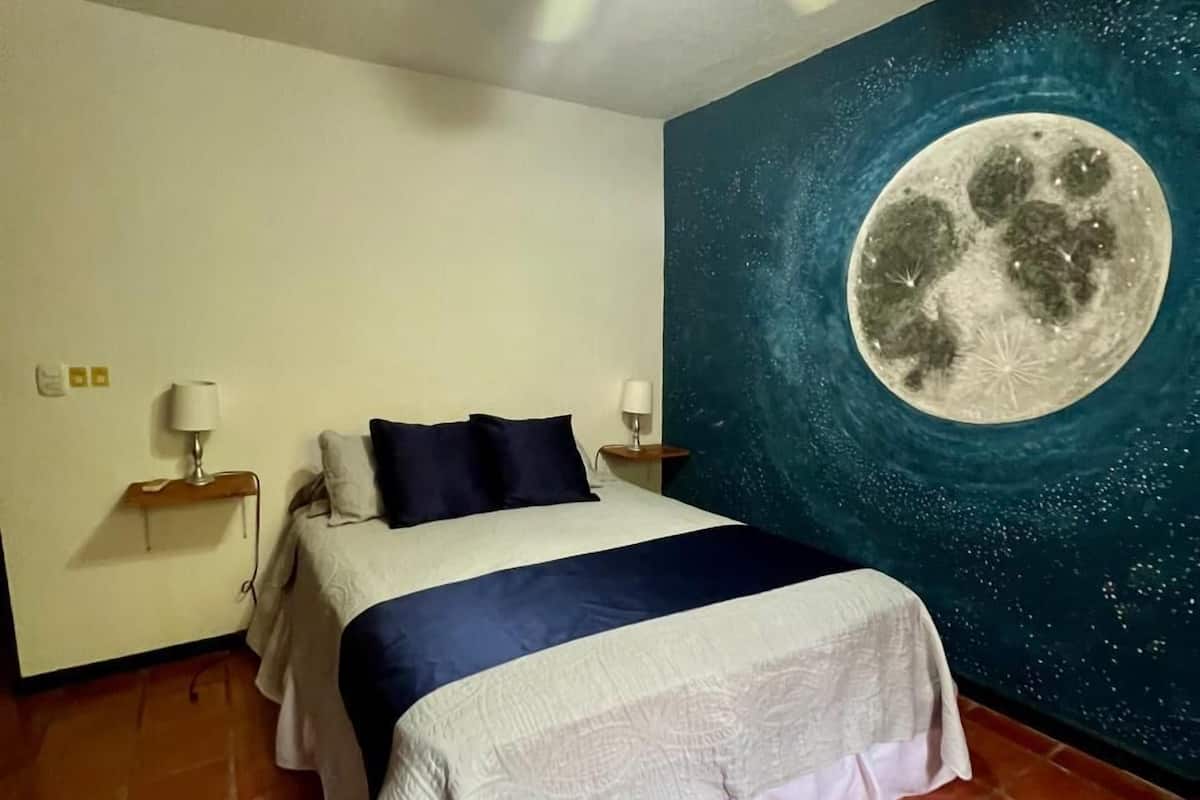A bedroom with a bed, a ceiling fan, a night sky mural with a moon, and tiled flooring.