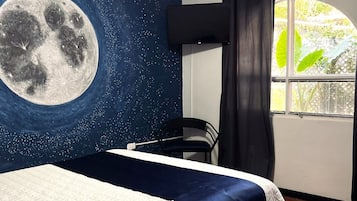 Une chambre à coucher comprenant un lit, un ventilateur de plafond, une fresque murale représentant la lune, une fenêtre avec des rideaux et une chaise.