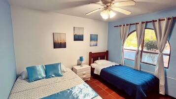 Une chambre avec deux lits, un ventilateur de plafond, une table de chevet et une fenêtre avec des rideaux.