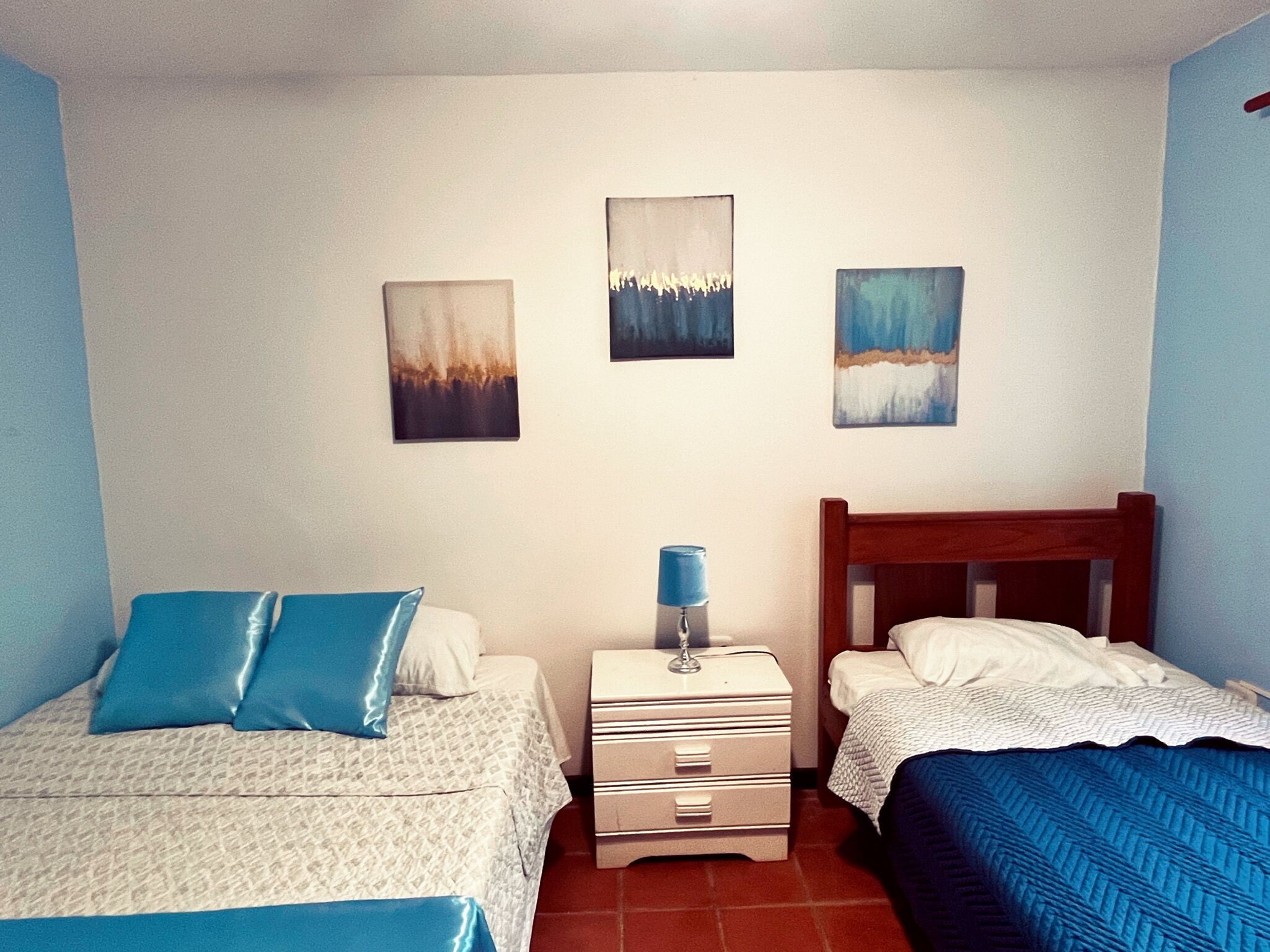 Une chambre avec deux lits, une table de chevet et trois tableaux accrochés au mur.