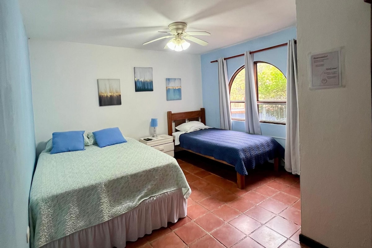 A bedroom with two beds, a ceiling fan, a nightstand, and a window with curtains.