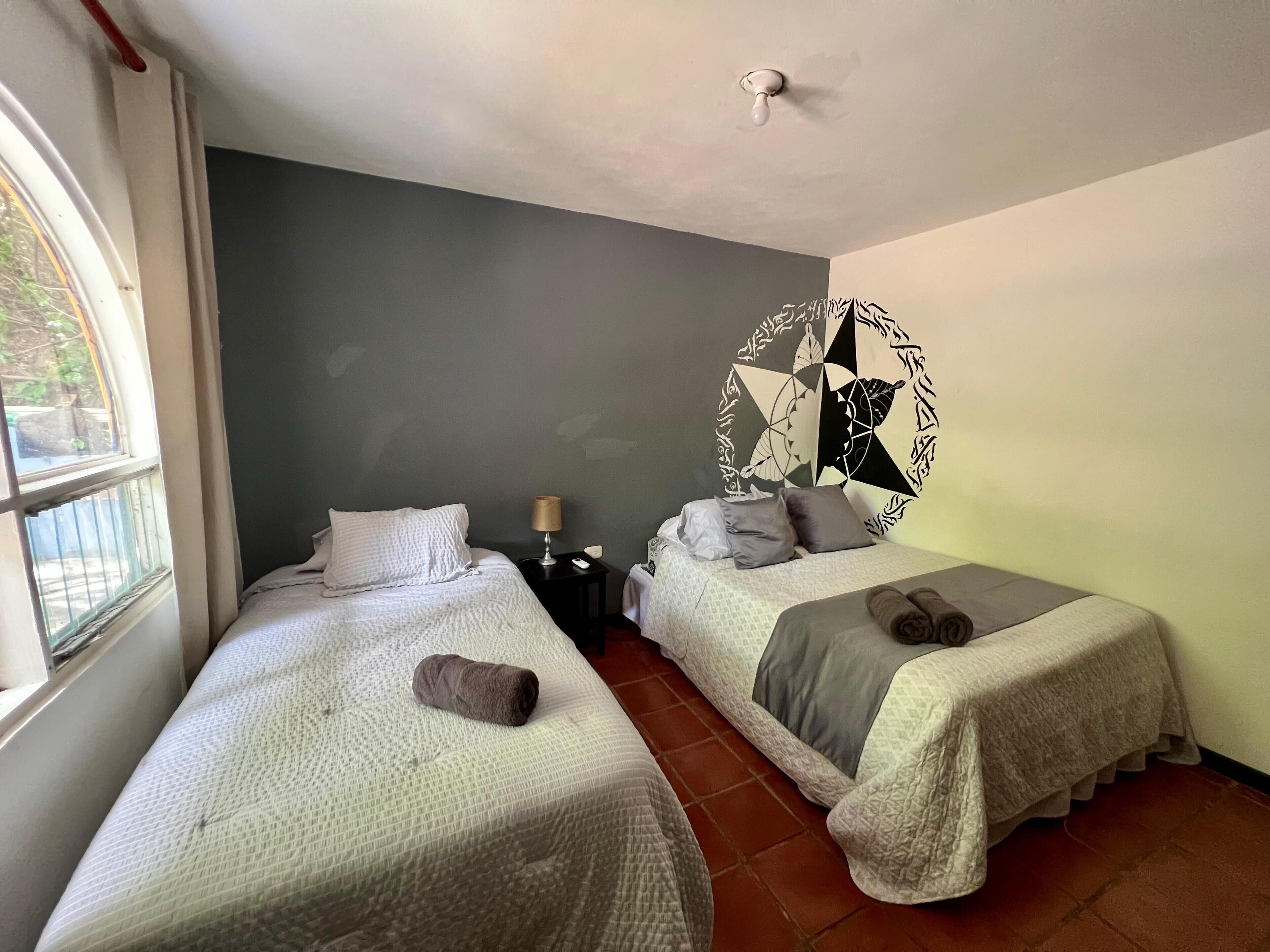 Une chambre avec deux lits, une table de chevet, une lampe et un élément décoratif mural.