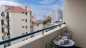Varanda com mesa posta para dois, com vista para uma área residencial com edifícios e céu claro.