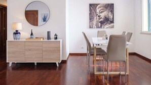 Uma área de refeições com uma mesa branca, duas cadeiras, um armário de madeira e um espelho redondo na parede.