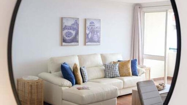 Uma sala de estar com sofá, almofadas, mesa lateral e espelho na parede.
