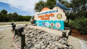 A welcome sign for Holmes Beach on Anna Maria Island with a dolphin sculpture and various logos.