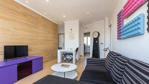 Un salon moderne avec un meuble de rangement pour appareils multimédias de couleur violette, un canapé noir, une table basse blanche et un mur d’accent en bois.