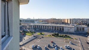 Une vue d’un parking avec plusieurs voitures, d’un grand bâtiment doté de colonnes et d’un ciel dégagé.
