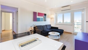 Un salon moderne avec un canapé noir, une table basse blanche et une œuvre d’art murale aux couleurs vives.