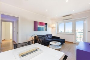 Un salon moderne avec un canapé noir, une table basse blanche et une œuvre d’art murale aux couleurs vives.