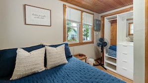 A bedroom with a bed, a bedside table, a fan, a wardrobe, and a window with blinds.