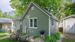 A single-story house with a gabled roof, a front porch with two chairs, and a barbecue grill in the yard.