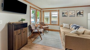 A living room with a TV, wooden furniture, a sofa, and a window with a view.