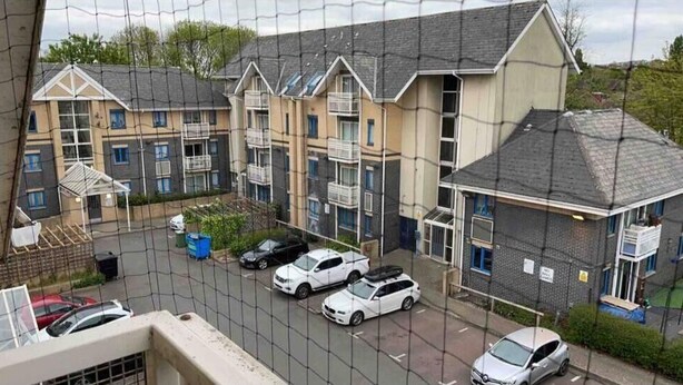 Un edifici residencial amb nombroses balconades, una zona d'aparcament amb diversos cotxes i una petita zona verda.