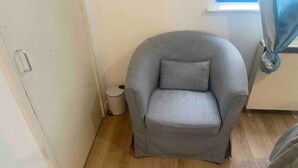 Una armchair gris amb un coixí en un espai amb sòls de fusta i una finestra amb cortines.