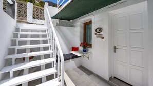 Un escalier blanc menant à une porte dotée d’une petite fenêtre et surmontée d’un coussin rouge.