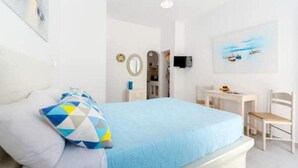 Une chambre à coucher avec un lit, un bureau et une chaise. Il y a un tableau accroché au mur et un téléviseur fixé au mur.