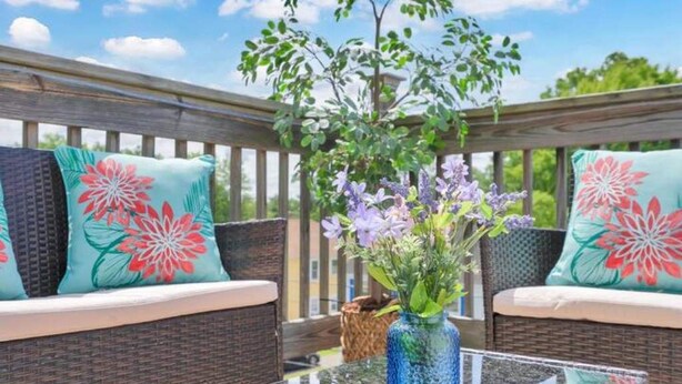 Ein Korbsessel mit floralen Kissen, ein Glastisch und eine Vase mit Blumen auf einer Terrassenfläche.