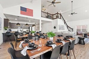 A spacious dining area with a long wooden table set for a meal, a kitchen in the background, and a staircase leading to an upper level. - Crane’s Nest-Year Round Private Pool & Hot Tub (kimberling City)