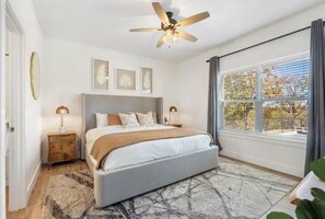 A bedroom with a bed, a ceiling fan, a window with curtains, and framed artwork on the wall. - Crane’s Nest-Year Round Private Pool & Hot Tub (kimberling City)
