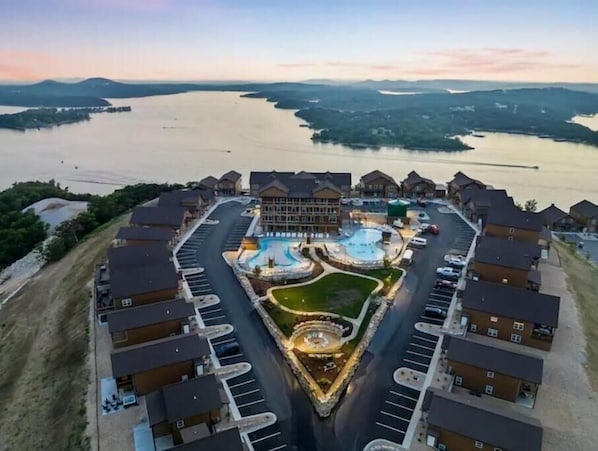 Un resort con piscina central, varias construcciones y vistas a un lago.