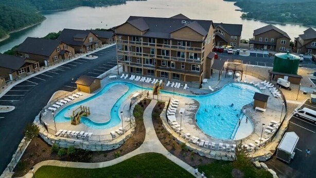 A hotel with a large swimming pool, a parking lot, and a view of a river.