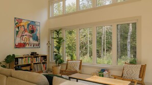 Una sala de estar acogedora con un ventanal grande, una estantería y un cuadro de colores.