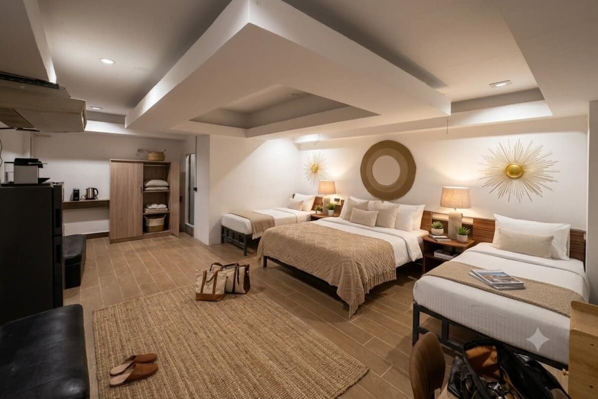 Ein modernes Hotelzimmer mit zwei Betten, einer Küchenzeile, einem großen Spiegel und einer Wanddekoration mit Sonnenstrahlen.