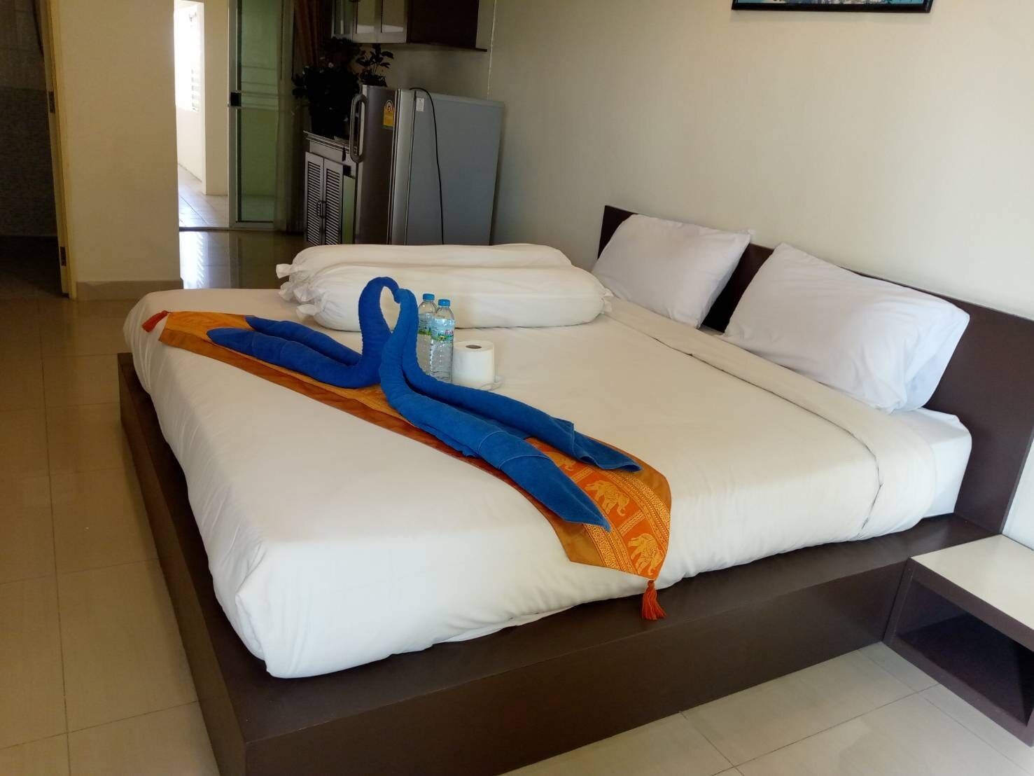 Habitación de hotel con dos camas, una mesita y una pequeña cocina.