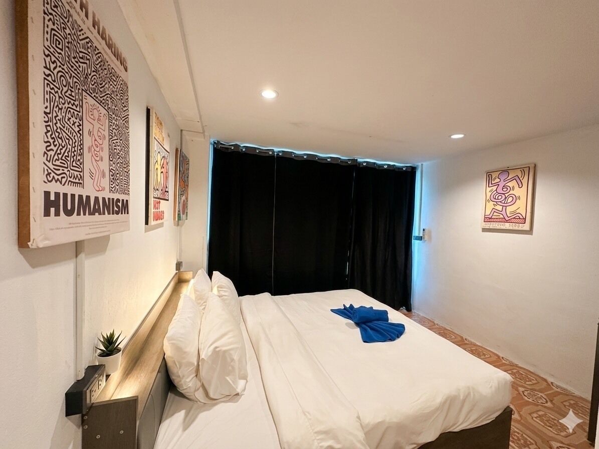 Una habitación de hotel con una cama, una mesita de noche, un reloj en la pared y una cortina.