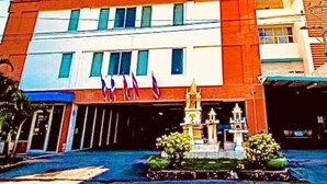 A multi-story building with a prominent entrance, a small garden area with statues, and several flags. - Navanakorn Aomsin Hotel near Big C Super (Khlong Luang)