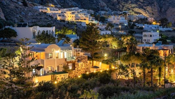 A coastal village at dusk with white buildings, some with domed roofs, surrounded by greenery and a rocky hillside. - MOSCHATOS BEACH HOUSE (Καμάρι)