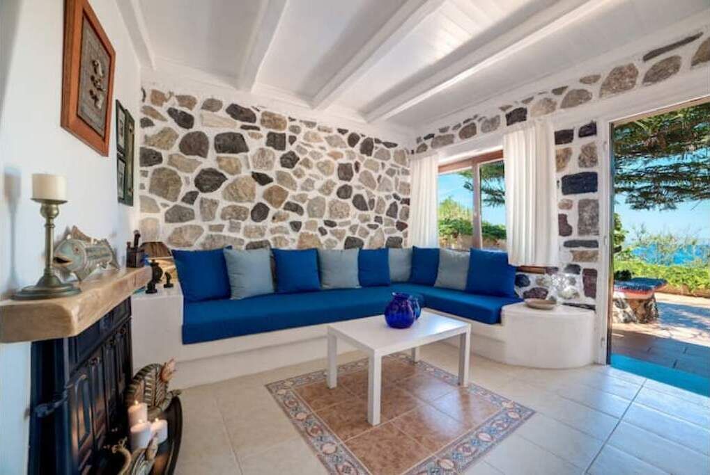 Un soggiorno con parete in pietra, divano blu, tavolino da caffè bianco e camino.