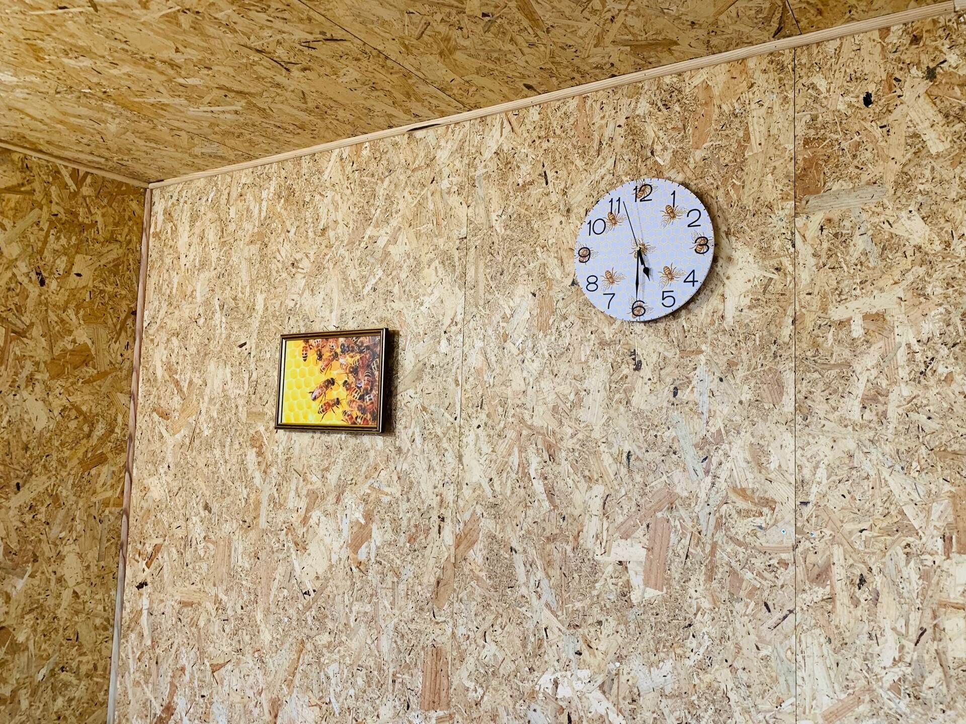 Ein Zimmer mit einer Holzwand, einer Uhr und einem gerahmten Bild von Bienen.